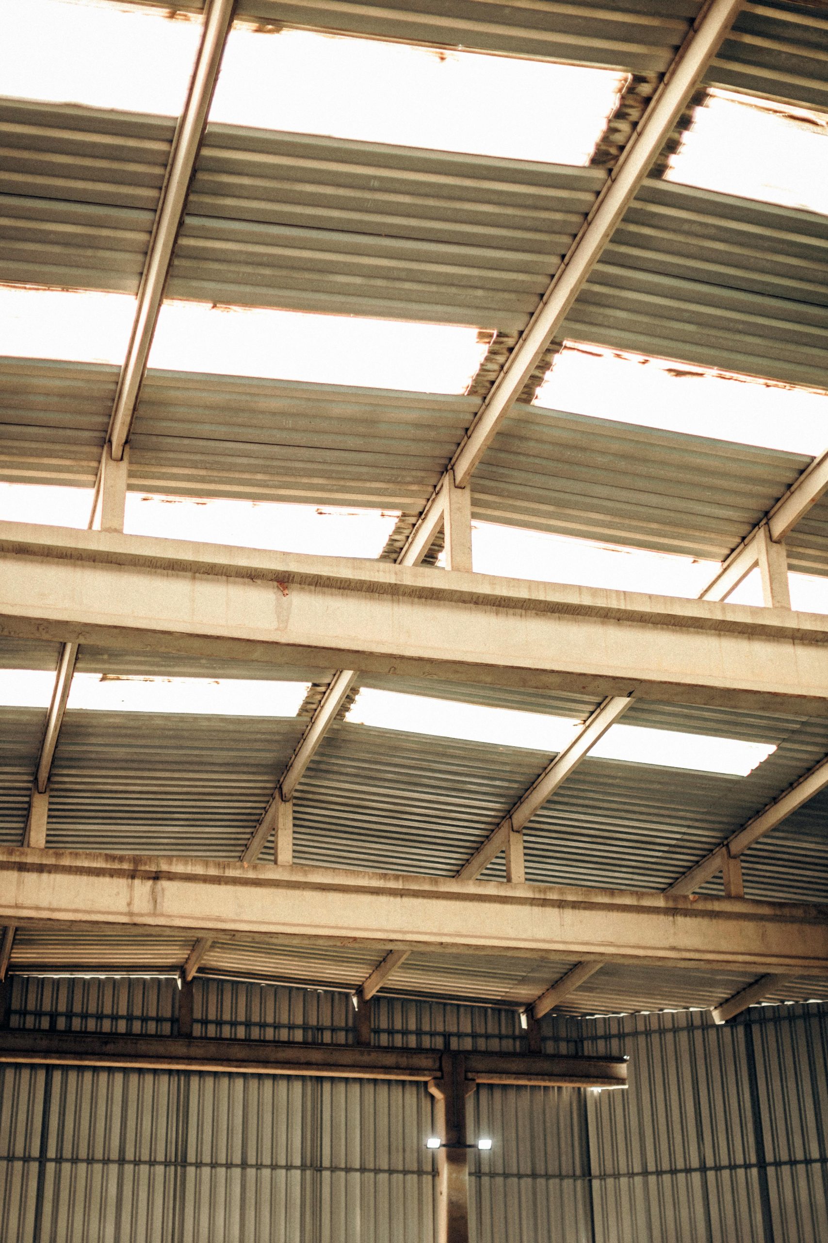 View of a spacious industrial warehouse ceiling with visible steel beams and corrugated panels.